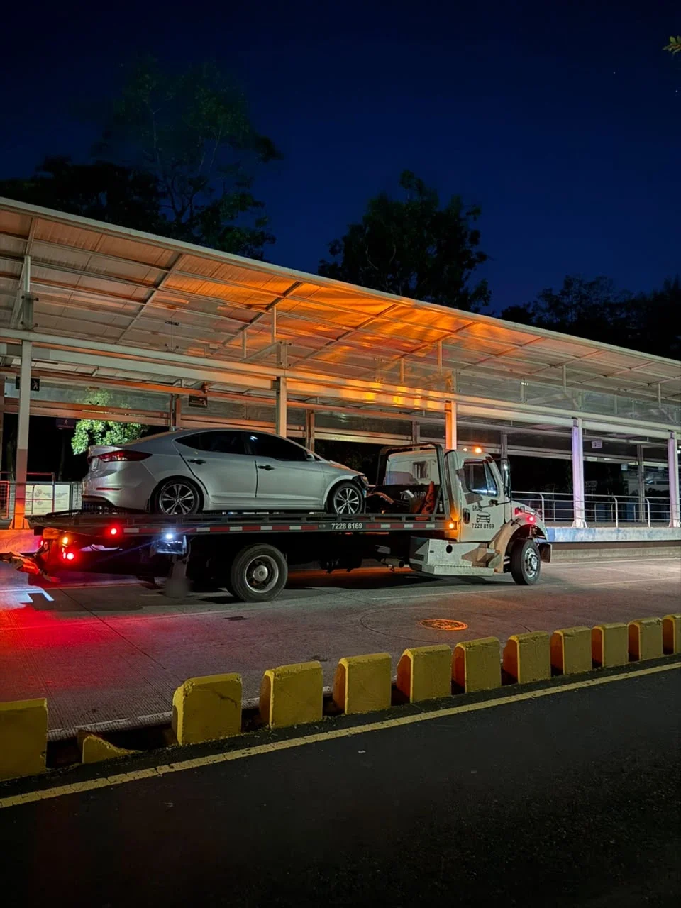 Traslado nocturno de un sedán plateado en grúa de plataforma