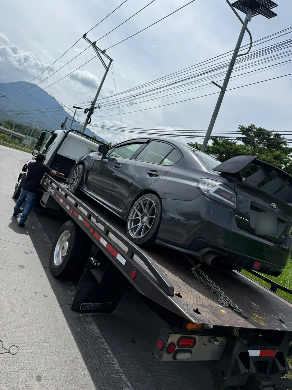 Operador asegurando un Subaru gris en la plataforma de la grúa